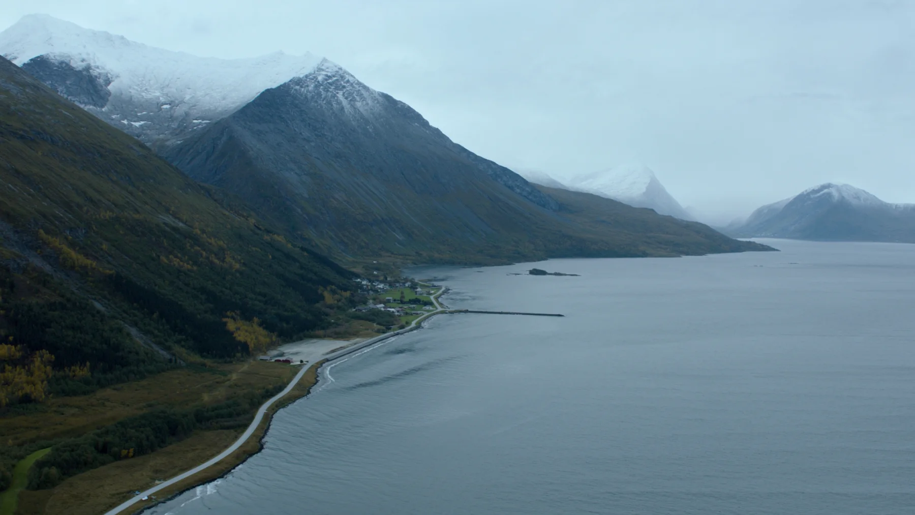 Lyngenfjorden sett ovenfra i september, kystvei og gårder langs stranda, nysnø på toppene